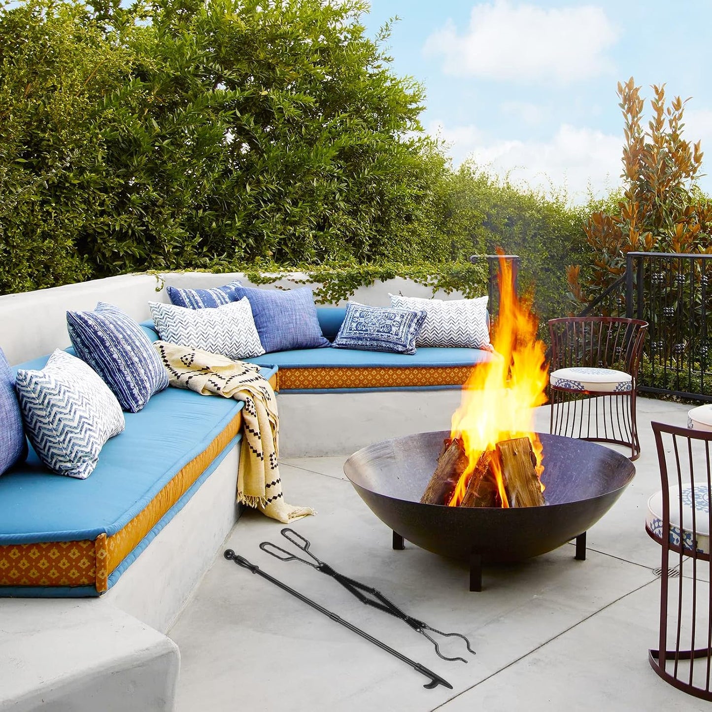 Black metal fireplace poker and tongs set laid out next to an outdoor fire pit on a patio