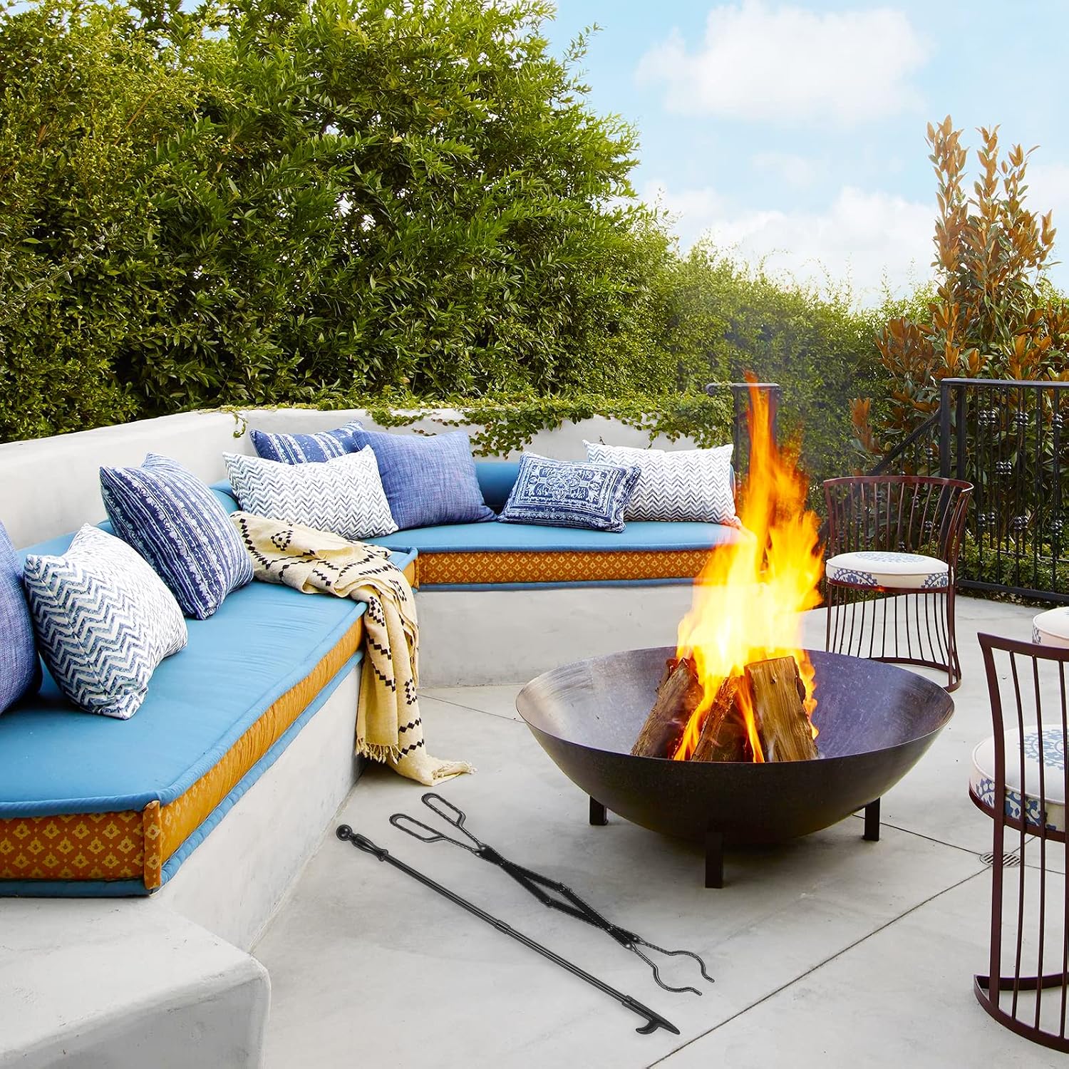 Black metal fireplace poker and tongs set laid out next to an outdoor fire pit on a patio