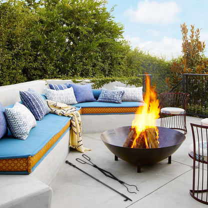 Black metal fireplace poker and tongs set laid out next to an outdoor fire pit on a patio