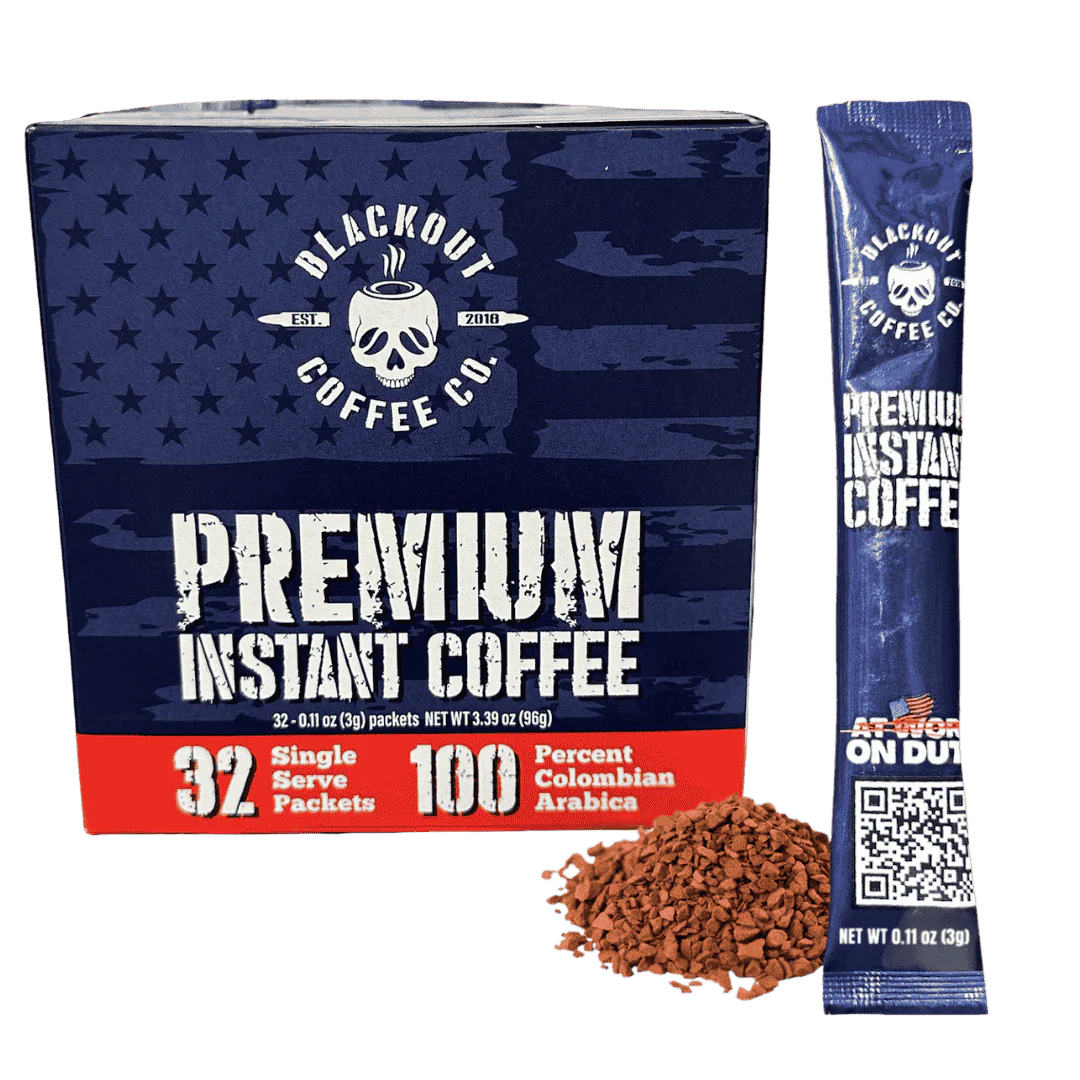 Blackout Coffee instant coffee single serve packs laid out on a rugged outdoor surface with an American flag in the background