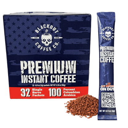 Blackout Coffee instant coffee single serve packs laid out on a rugged outdoor surface with an American flag in the background