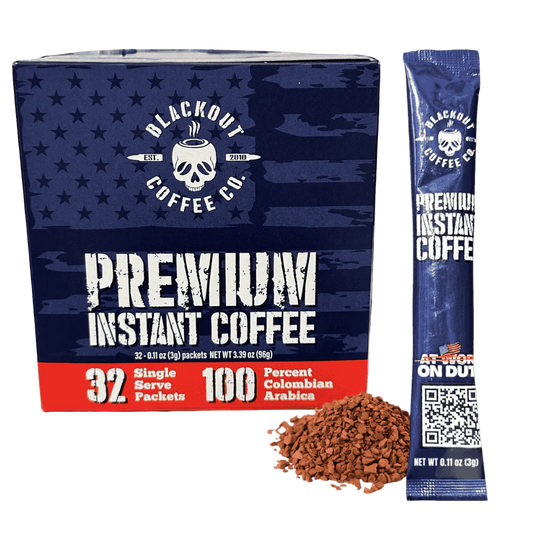 Blackout Coffee instant coffee single serve packs laid out on a rugged outdoor surface with an American flag in the background
