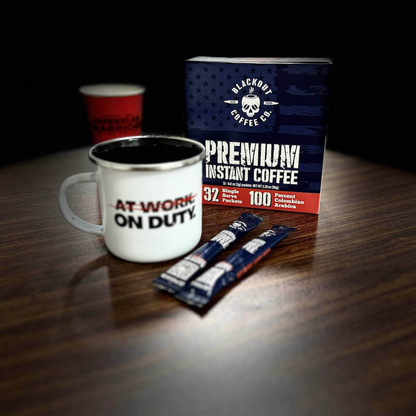 Blackout Coffee instant coffee single serve packs laid out on a rugged outdoor surface with an American flag in the background